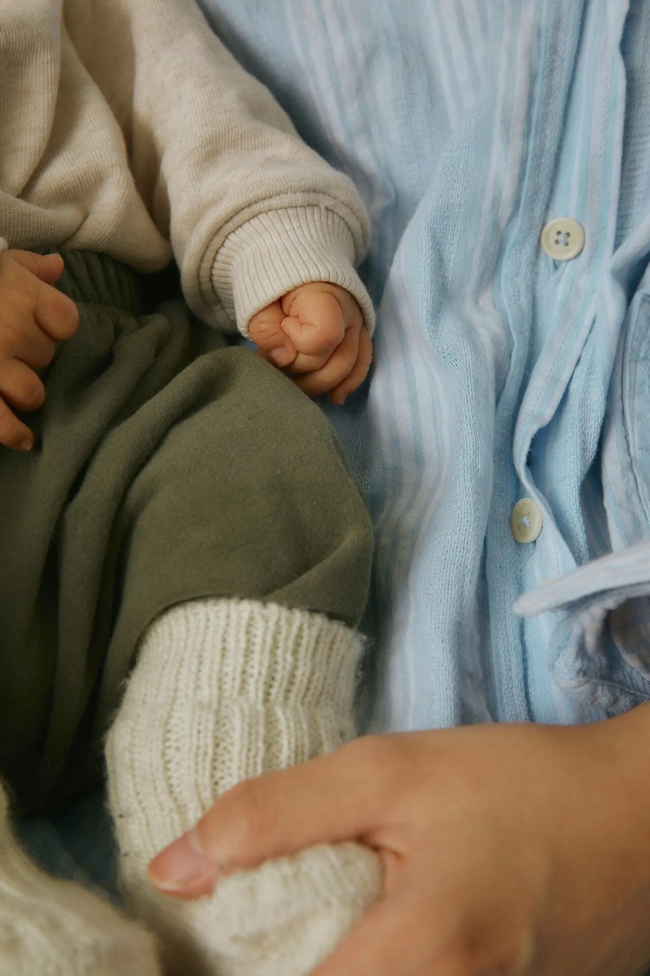 A baby's hand in a knitted sleeve holding an adult's hand