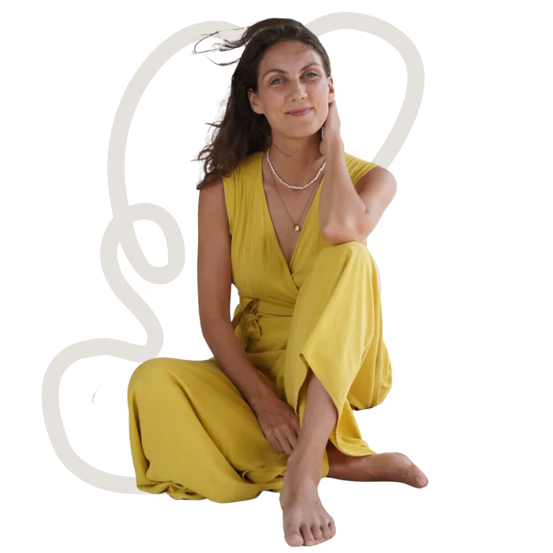 Kristin sitting barefoot in a yellow jumpsuit, one hand at her neck