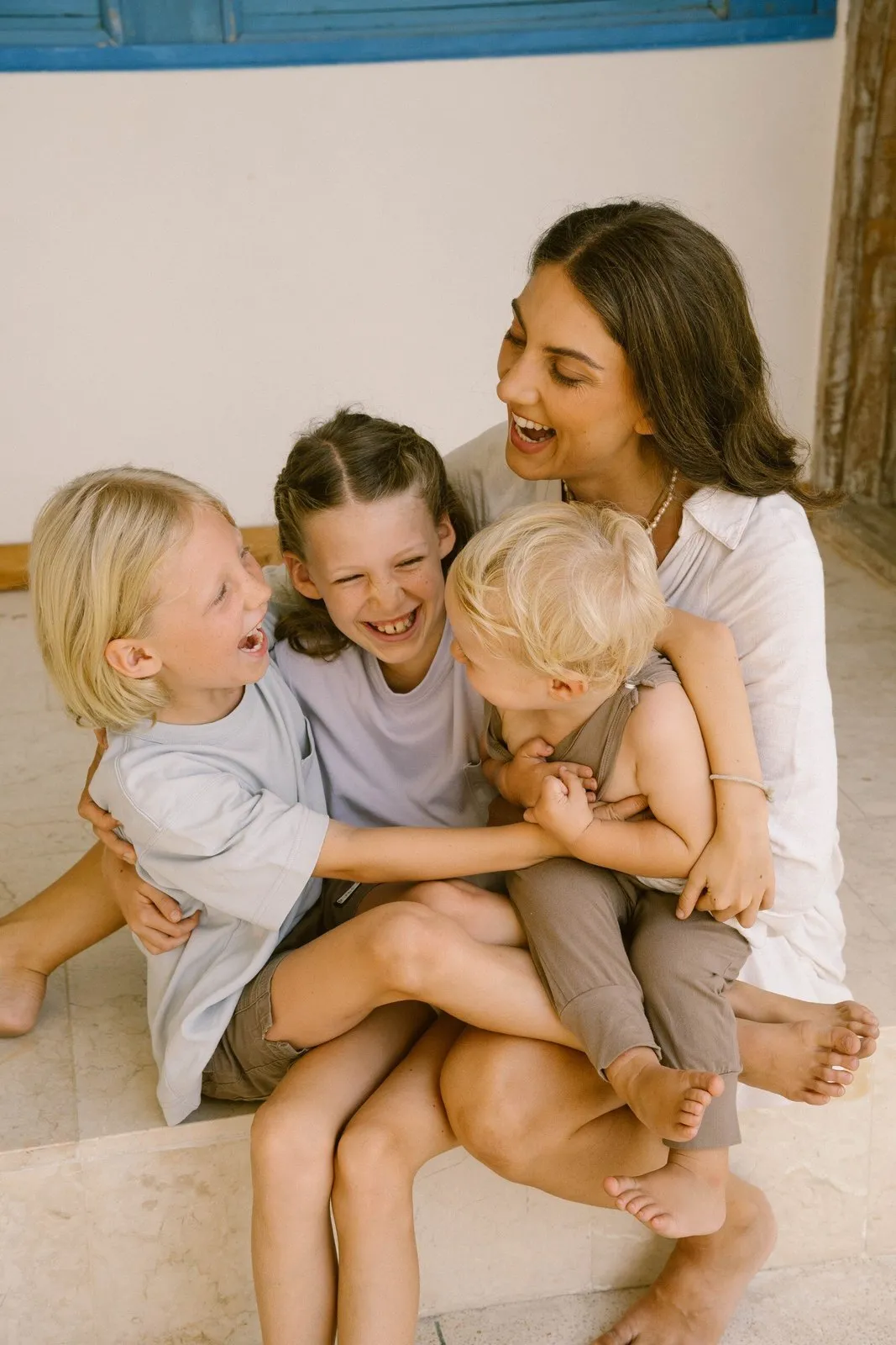 Kristin laughing on the floor with her three children piled on her lap