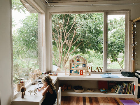 Girl sitting on a chair at a small desk writing near a window